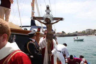 Il Crocifisso con raggiera sollevato a bordo di un'imbarcazione, con marinai e sacerdoti, e la costa con barche al seguito sullo sfondo