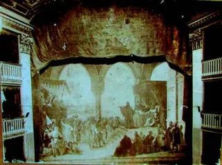 Foto d'epoca del boccascena del Teatro comunale di Trani con i palchi laterali e il sipario dipinto calato, raffigurante una scena medievale sotto una loggia gotica