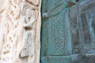 Dettaglio dello stipite in pietra scolpita con una figura e della porta in bronzo con formelle decorate del portale della Cattedrale