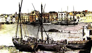 Foto d'epoca colorata a mano con velieri da pesca in secca e ormeggiati lungo la banchina, con le case del fronte porto sullo sfondo