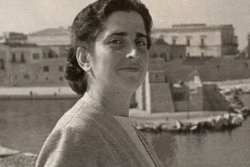 Ritratto in bianco e nero di Pina Salvati, giovane donna dai capelli scuri, con alle spalle un porto e i suoi palazzi