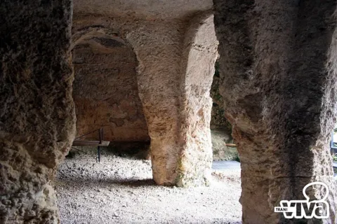 Pilastri e archi ricavati nella roccia nella penombra dell'ipogeo di Santa Geffa