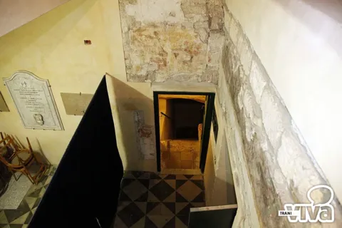 Scala che scende a un ambiente inferiore, con una lapide commemorativa sulla parete