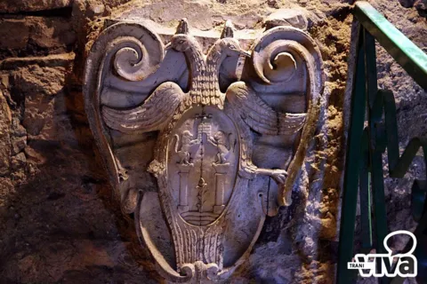 Stemma in pietra con aquila bicipite e scudo, murato in una parete di pietra grezza