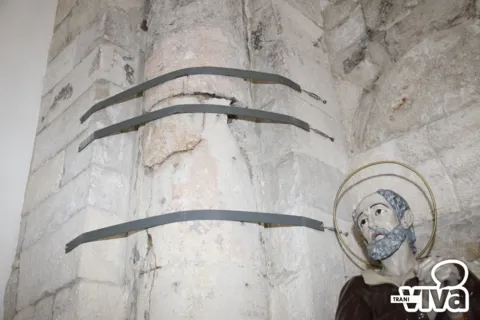 Una colonna stretta da staffe di ferro e la statua di un santo anziano con aureola