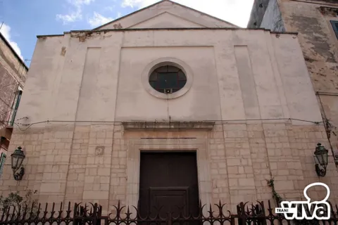 Facciata della chiesa di San Toma: timpano, finestra circolare, portale in legno, due lanterne e cancellata in ferro