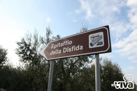 Cartello turistico marrone con freccia e la scritta «Epitaffio della Disfida», fra gli ulivi