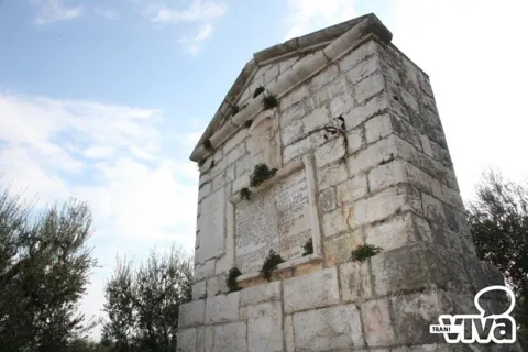 Il monumento di scorcio, con la lapide latina sulla facciata e piante cresciute fra le pietre