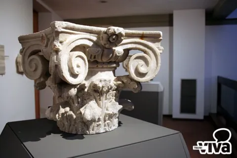 Capitello in pietra con volute e foglie d'acanto, esposto su un piedistallo grigio