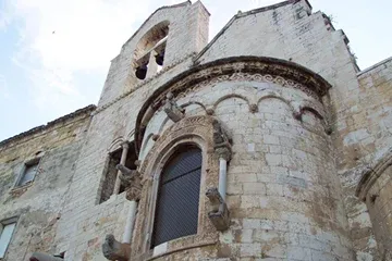 Abside romanica in pietra della chiesa di Ognissanti, con finestra ad arco, mensole scolpite e campanile a vela