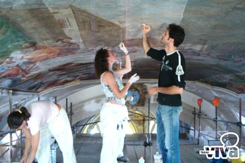 Restauratori su un'impalcatura al lavoro sull'affresco della volta, con guanti e strumenti