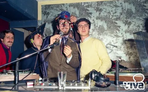 Ragazzi dietro una consolle da dj; uno, con occhiali e un cappello da festa, parla al microfono