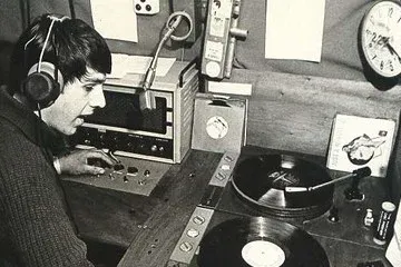 Ragazzo con le cuffie al microfono tra giradischi e dischi in uno studio radiofonico, foto in bianco e nero