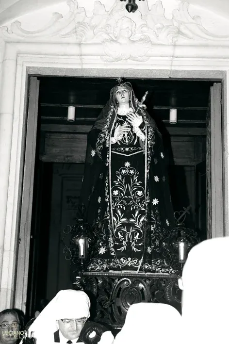 La statua dell'Addolorata, con manto nero ricamato e lanterne, esce dal portale di una chiesa