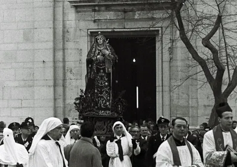 La statua dell'Addolorata esce dal portale di una chiesa, accompagnata da confratelli in bianco, sacerdoti con stola e carabinieri in alta uniforme