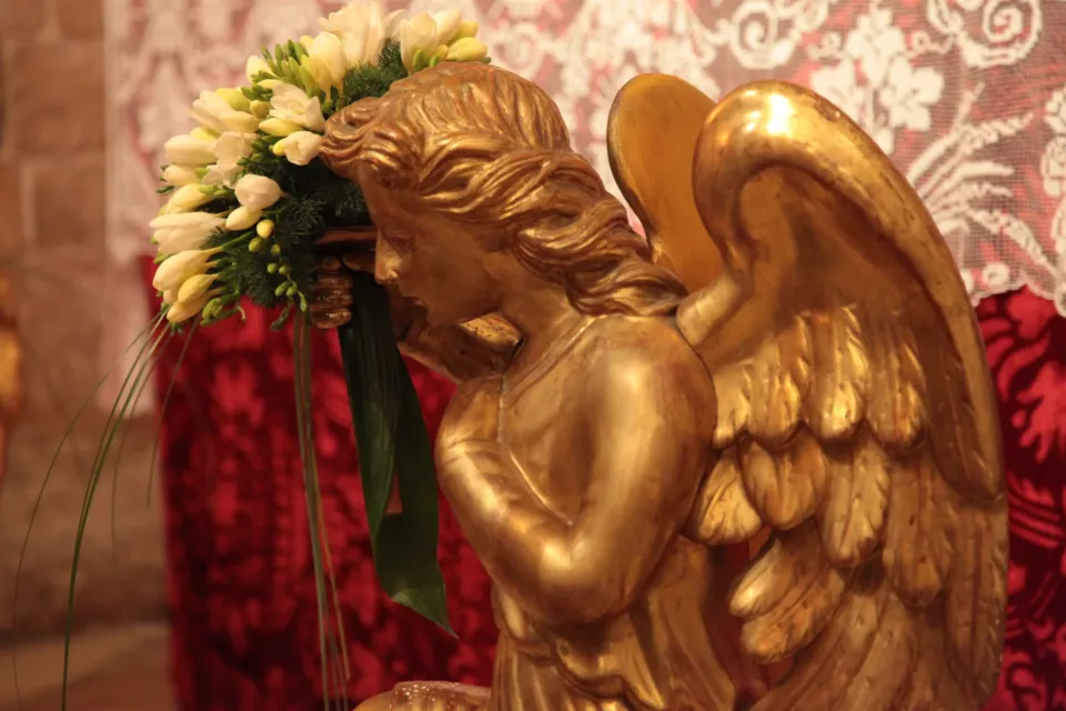 Dettaglio di un angelo ligneo dorato che regge un mazzo di fiori bianchi davanti a un drappo rosso, nell'allestimento del Giovedì Santo