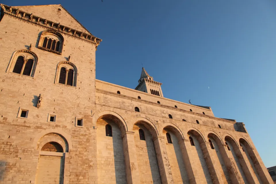 Il fianco della Cattedrale con le alte arcate cieche e le bifore, ripreso dal basso nella luce calda del tardo pomeriggio contro il cielo blu