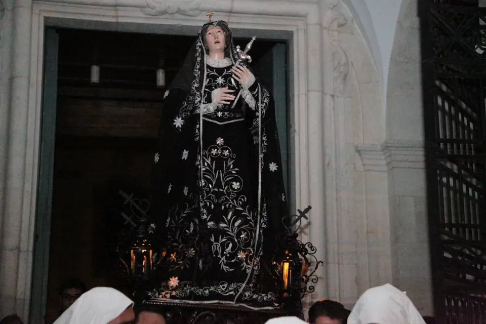 La statua dell'Addolorata con manto nero ricamato d'argento e pugnale al petto esce da un portale tra confratelli incappucciati