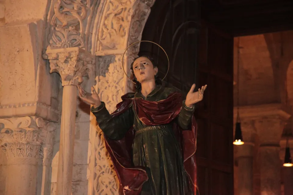 La statua di San Giovanni apostolo con aureola e mantello rosso, in gesto di dolore, presso il portale romanico della chiesa