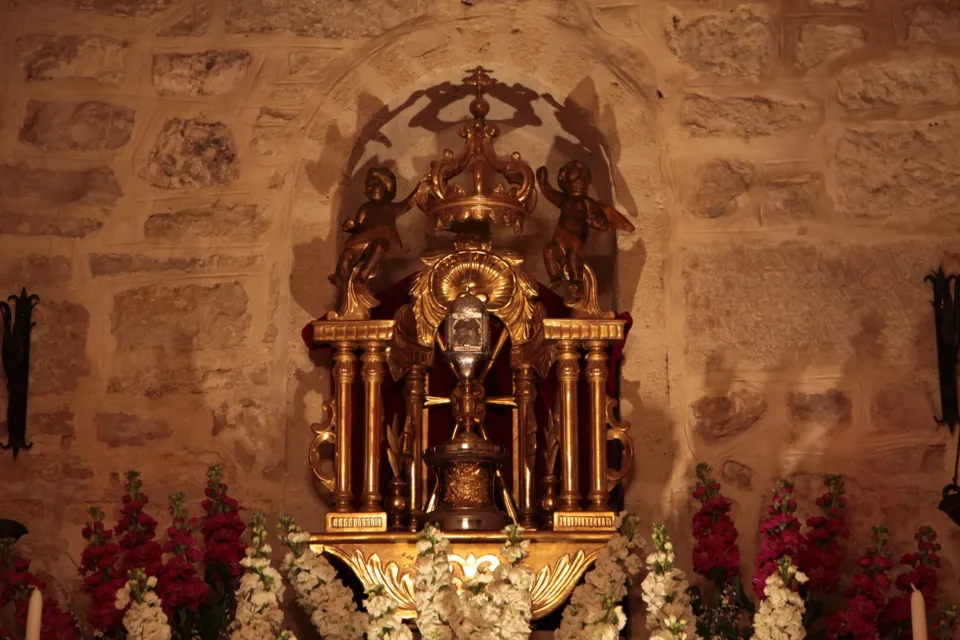 Un ostensorio dorato su un tempietto barocco, circondato da fiori bianchi e rossi, in una cappella dalle pareti in pietra