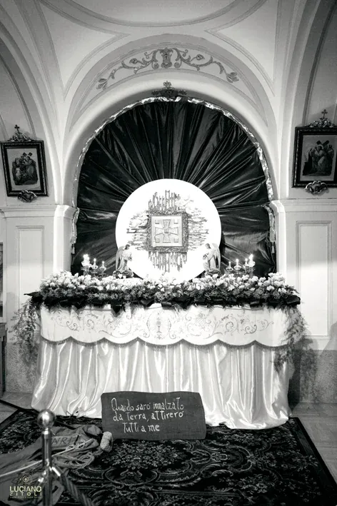 Altare con drappeggi, fiori, candele e un cartello con un'iscrizione, allestito sotto un arco in una chiesa