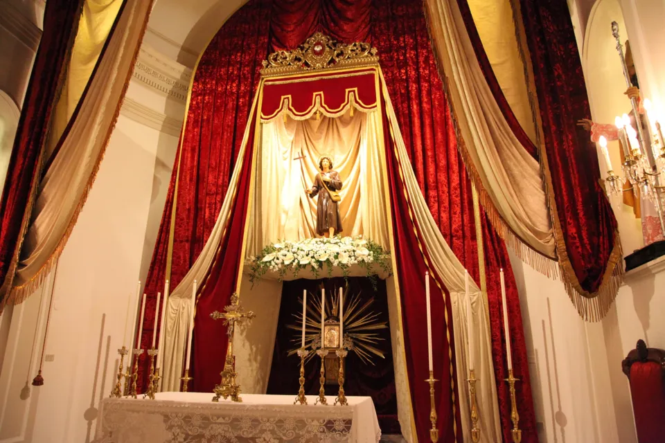 Altare allestito con una statuetta di San Nicola Pellegrino sotto un baldacchino di drappi rossi e bianchi, con candelieri e fiori