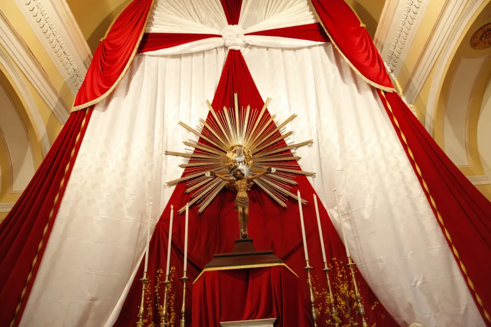 Altare con raggiera dorata e crocifisso, incorniciato da drappi rossi e bianchi, allestito per la festa del Crocifisso