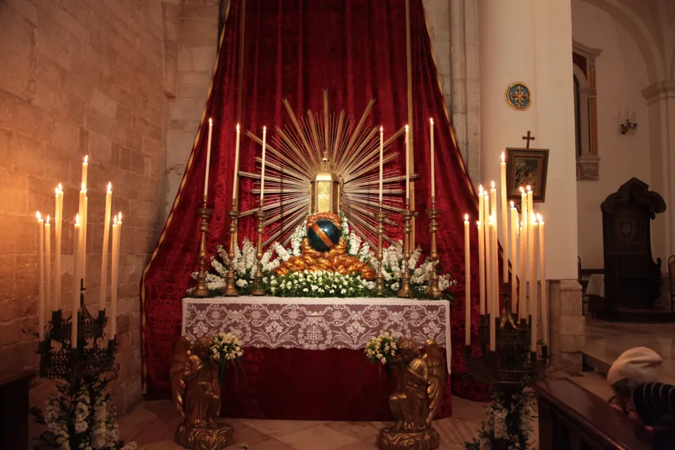 Altare con raggiera dorata, candelabri e fiori sotto un baldacchino di drappi rossi, allestito per il Giovedì Santo