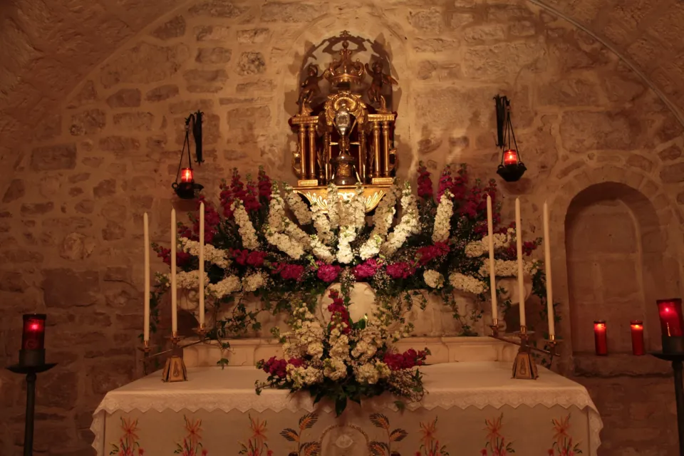 Altare addobbato con composizioni di fiori bianchi e rossi, candele e lumini rossi, sotto un tabernacolo dorato in una cappella in pietra