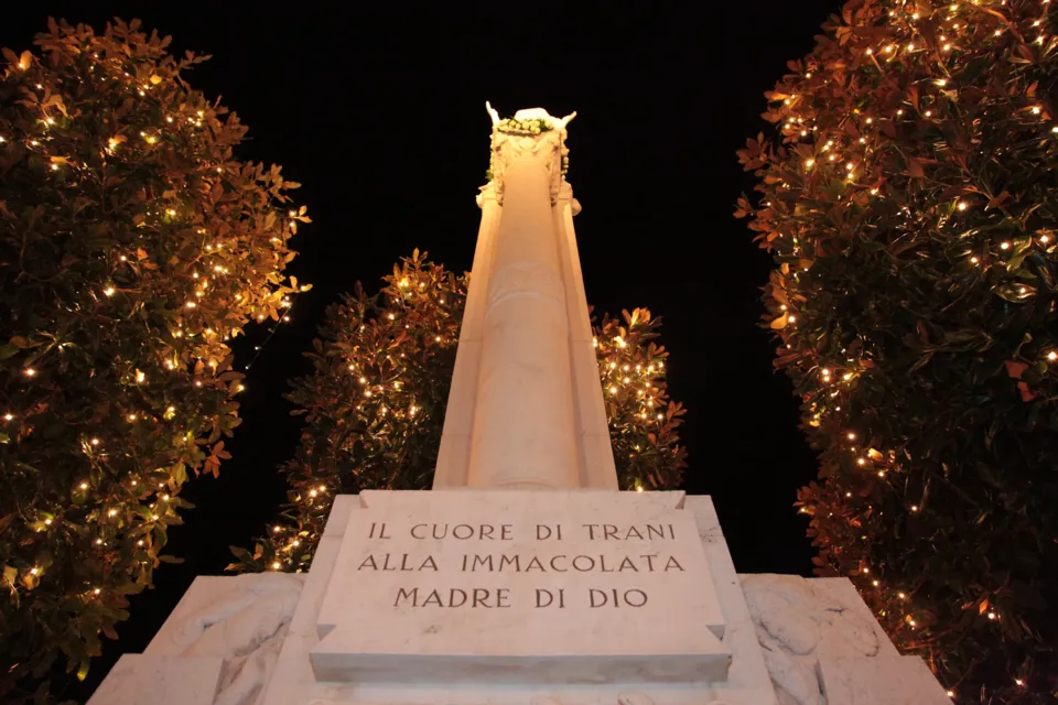 Colonna dell'Immacolata illuminata di notte; sulla base l'epigrafe 'Il cuore di Trani alla Immacolata Madre di Dio', ai lati alberi con luci
