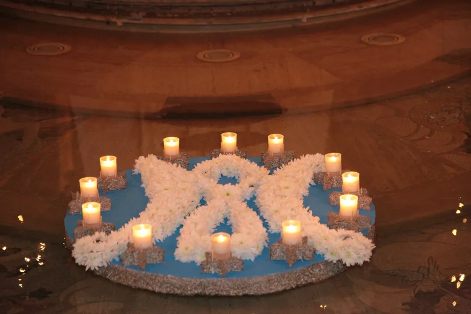 Composizione galleggiante di fiori bianchi a forma di monogramma mariano con candele accese, sull'acqua della fontana alla base del monumento all'Immacolata