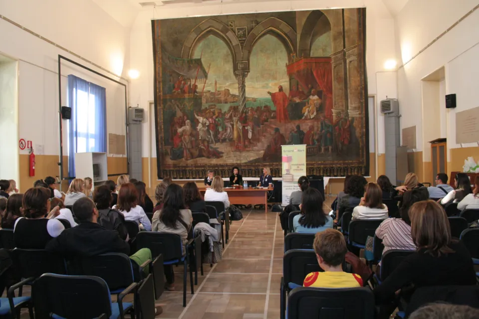 Sala con pubblico seduto e tavolo dei relatori, sotto il grande sipario dipinto del Teatro comunale appeso alla parete di fondo