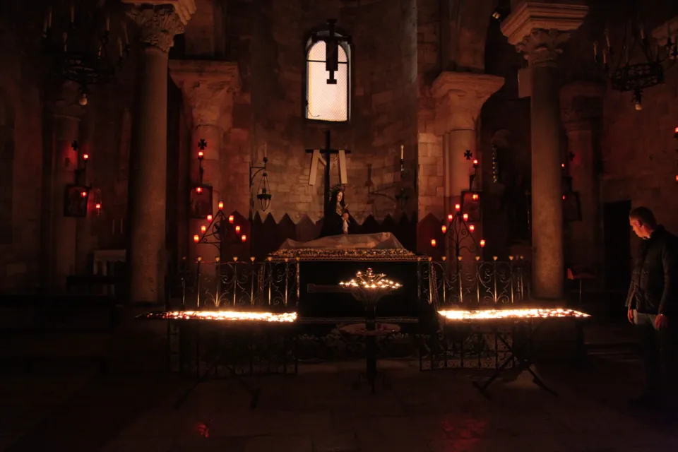 Interno scuro di una chiesa a colonne con file di lumini accesi a terra e un sepolcro al centro, durante la notte del Giovedì Santo