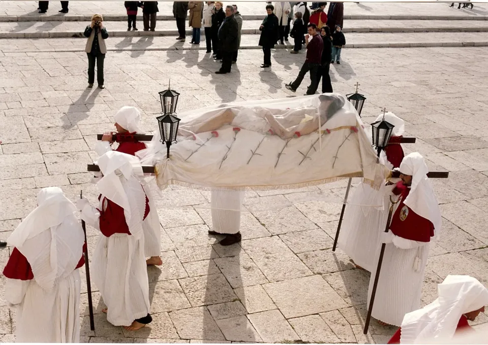 Il simulacro del Cristo morto coperto da un velo trasparente, portato su una lettiga con lanterne da confratelli in bianco con mozzetta rossa, su una piazza lastricata