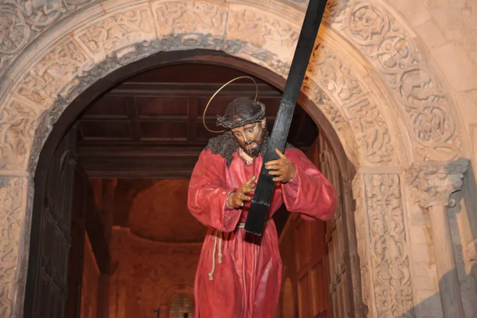 La statua di Gesù che porta la croce, in tunica rossa, esce dal portale romanico decorato a girali della chiesa
