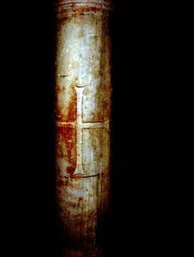 Fusto di colonna in pietra con una croce incisa, scontornato su fondo nero; probabile segno votivo lasciato da marinai