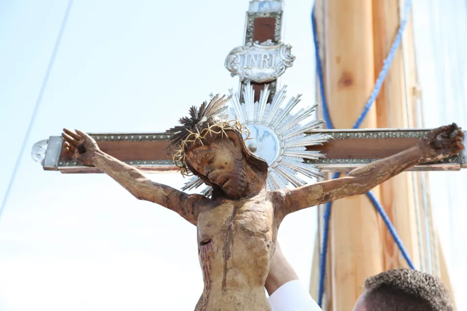 Il Crocifisso ligneo di Colonna con raggiera argentata, ripreso dal basso contro il cielo accanto all'albero della barca