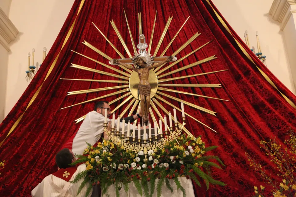 Il Crocifisso con grande raggiera dorata esposto sull'altare davanti a un drappo di velluto rosso, con candele e fiori; un sacerdote all'altare
