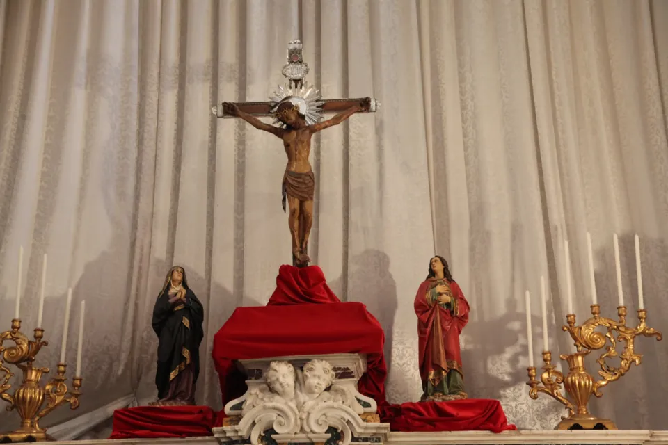 Il Crocifisso di Colonna collocato sull'altare davanti a un drappo chiaro, fra due statue di santi, candelabri dorati e un drappo rosso