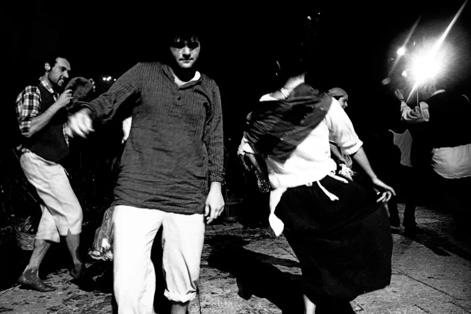 Ballerini in costume tradizionale danzano di notte, illuminati dal flash, in bianco e nero