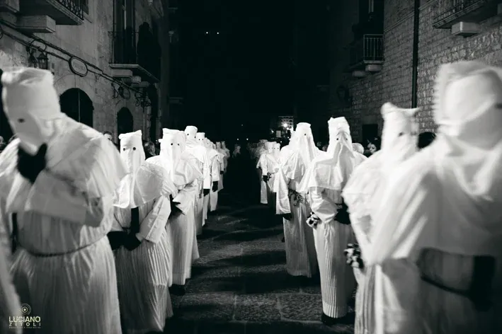 Due file di confratelli incappucciati in bianco percorrono di notte una strada del centro storico