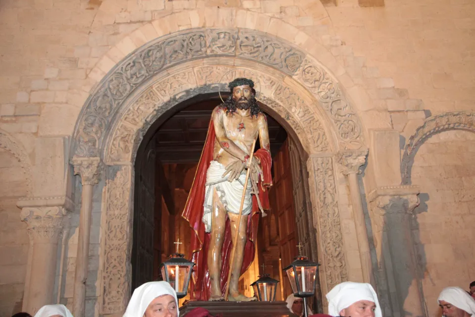 La statua dell'Ecce Homo con mantello rosso esce dal portale romanico con archivolto scolpito, portata da confratelli incappucciati