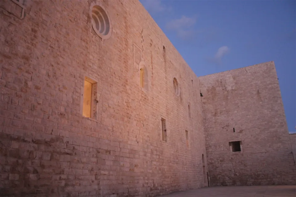 Parete del Castello Svevo con un oculo e finestre, in luce rosata del tramonto contro il cielo blu
