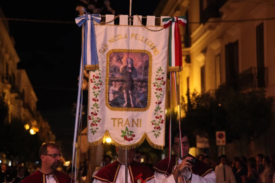 Gonfalone ricamato con l'immagine del santo e la scritta 'San Nicola Pellegrino Trani', portato di sera in processione tra i palazzi