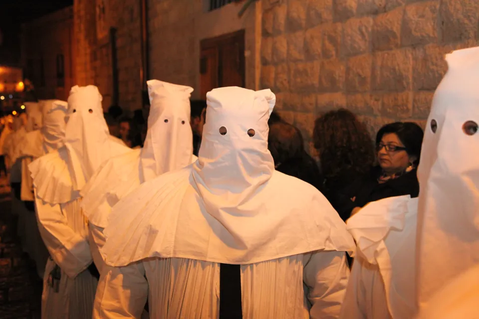 Confratelli con cappuccio bianco a punta e fori per gli occhi, in fila nella processione notturna in una via del centro storico