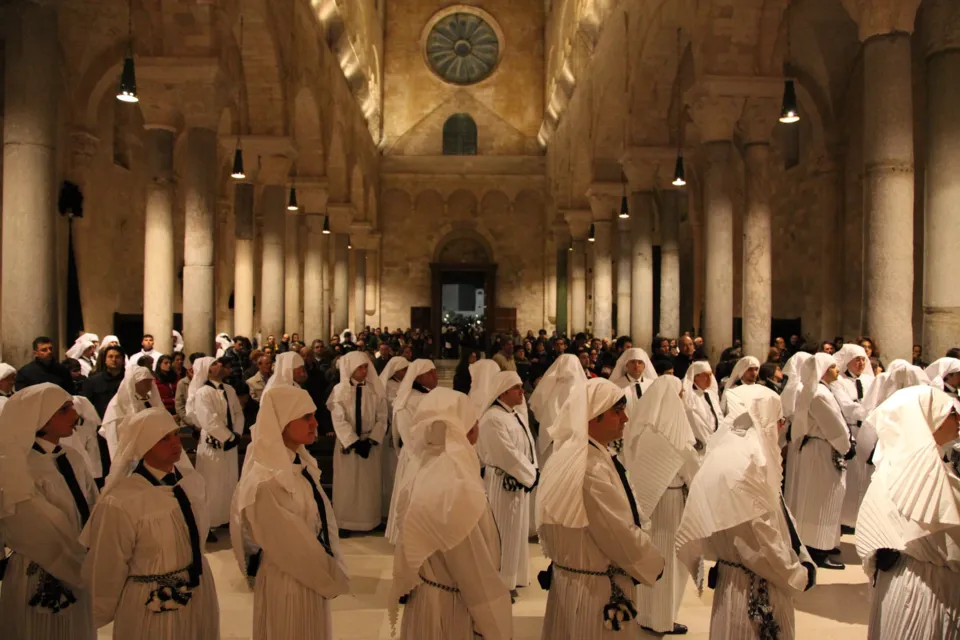 Centinaia di confratelli in saio e cappuccio bianco riempiono la navata della Cattedrale di Trani, con colonne binate e rosone sul fondo