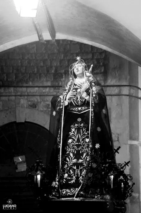 La statua dell'Addolorata con manto stellato e lanterne sotto un arco a volta in pietra, di notte