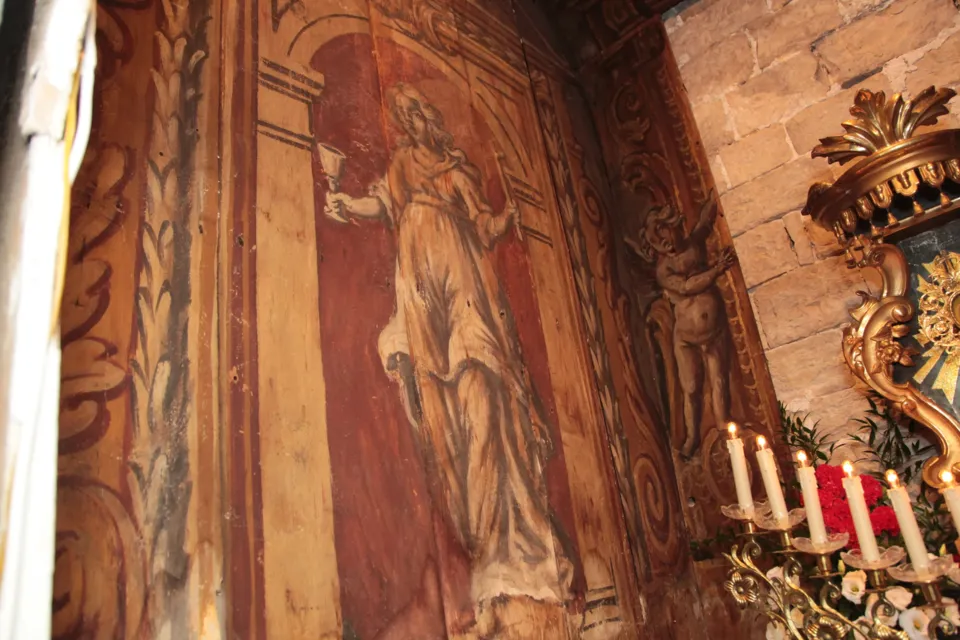 Dettaglio di un rivestimento ligneo dipinto con una figura femminile che regge un calice e un angelo, accanto a candele e cornice dorata