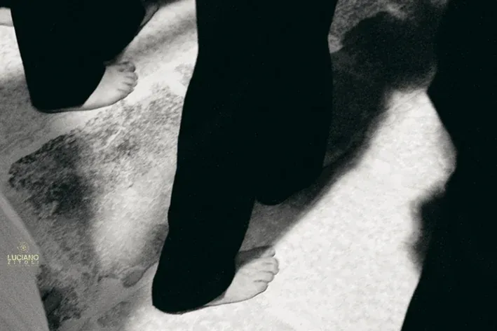 Primo piano dei piedi nudi di penitenti in veste nera che camminano sul selciato durante la processione