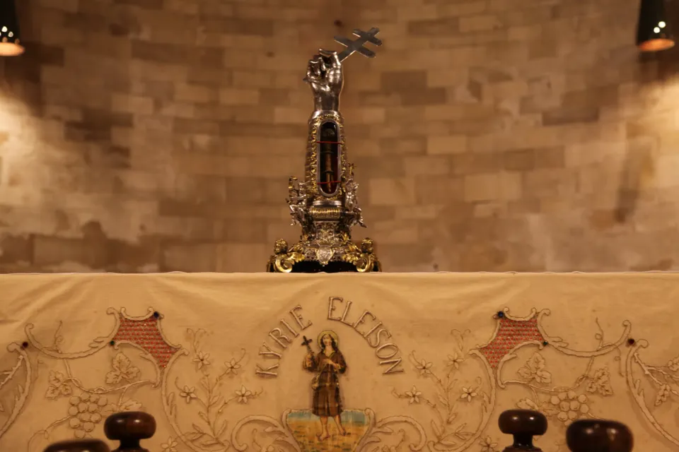 Reliquiario d'argento sormontato da una figura con croce, posto su un altare con paliotto ricamato con la scritta 'Kyrie Eleison' e l'immagine del santo